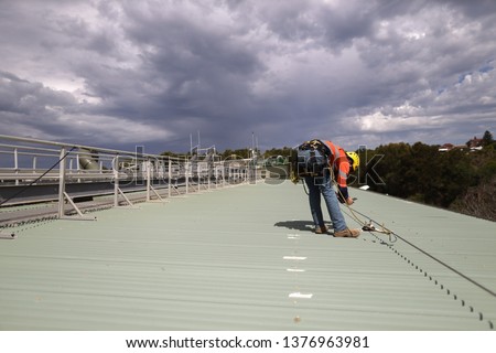 Rope access inspector technician using his phone taking pictures fall arrest, fall restraint roof anchor point
horizontal safety line while conducting safety inspecting Sydney, CBD, Australia   