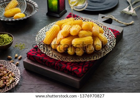 Arabic Cuisine:Pouring honey syrup on Middle Eastern traditonal dessert/Ramadan dessert "Balah Al-Sham" or "Balah El Shaam" .Oriental dessert place with pistachio and lanter. Close up with copy space. Royalty-Free Stock Photo #1376970827