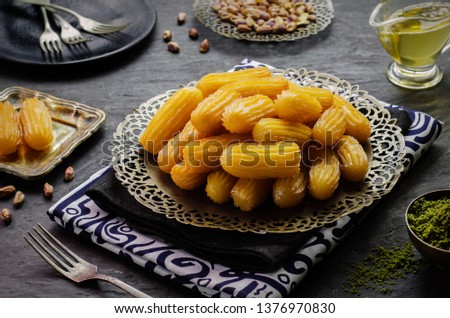 Arabic Cuisine: Middle Eastern traditonal dessert/Ramadan dessert "Balah Al-Sham" or "Balah El Shaam"  served with honey syrup and pistachio. Close up with copy space. Royalty-Free Stock Photo #1376970830