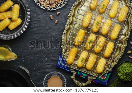 Arabic Cuisine: Middle Eastern Traditional dessert/Ramadan dessert Balah Al-Sham or Balah El Shaam served with pistachio, honey syrup and cup of tea and milk. Top view with copy sapce. Royalty-Free Stock Photo #1376979125