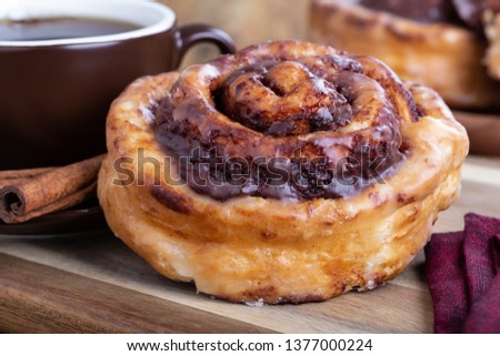 Closeup of a glazed cinnamon roll with a cup of coffee on a wooden surface