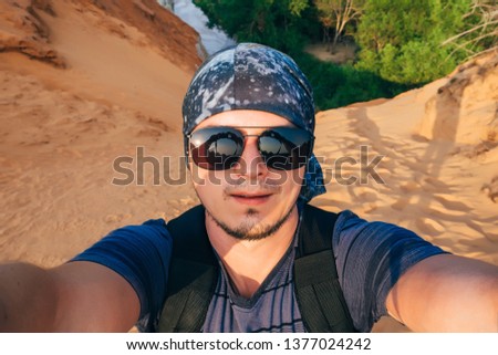 man Hiking with a backpack makes a selfie on the camera face in sunglasses and a bandana in the travel