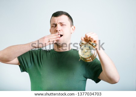 successful man yawns and stretches with an alarm clock, isolated on a gray background