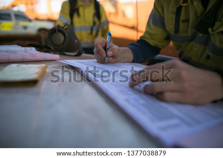 Miner supervisor inspecting and checking JSA risk assessment paper work permit making sure safety applying to the right job and sign its off prior to work on construction mine site, Perth, Australia