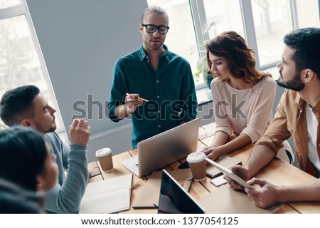 Searching for right decision. Top view of young modern people in smart casual wear discussing something while working in the creative office