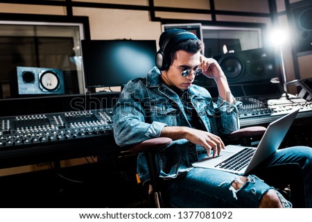 concentrated mixed race sound producer in headphones using laptop in recording studio Royalty-Free Stock Photo #1377081092