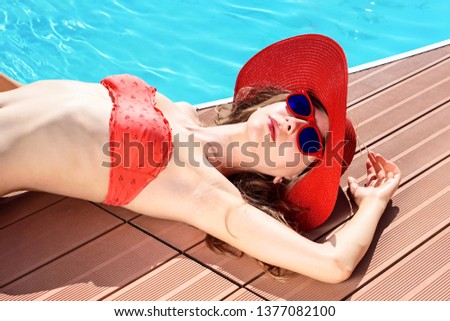 Beautiful young woman sun tanning at pool deck of cruise ship - Pretty girl on red bikini and sunglasses is sunbathing on yacht poolside - Summer holiday concept of skin care from sunburn - Image