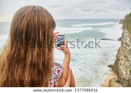 Young woman takes pictures on her phone. Girl taking pictures of a landscape. Bali, Uluwate. 
