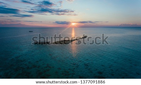 Beautiful sunset at the sea in Takat Sagele, Moyo Island, Sumbawa, Indonesia. Silhouette of a small island on a background of horizon separated orange and turquoise sky from the blue surface of water