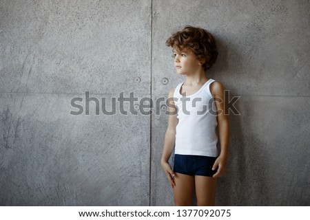 Profile portrait of a handsome little boy in underwear posing on concrete wall, looking a one side, copy space. Royalty-Free Stock Photo #1377092075