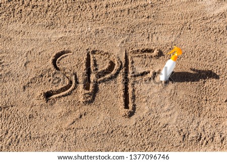 Sun protect factor. SPF word written on the sand and white bottle with suntan cream. Skin care concept background.