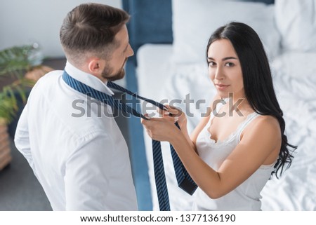 overhead view of beautiful woman tying tie of bearded man in bedroom 