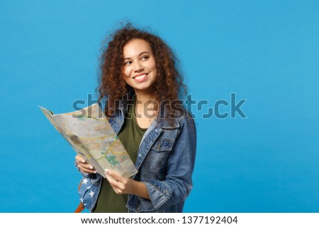 Young african american girl teen student in denim clothes, backpack hold map isolated on blue wall background studio portrait. Education in high school university college concept. Mock up copy space
