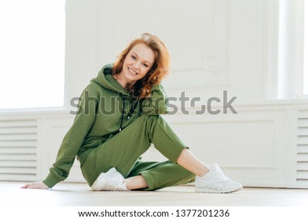 Delighted happy foxy woman busy with stretching pilate exercises in fitness studio, wears sportswear, has positive smile on face, enjoys workout, does cardio training. Acrobatics and sport concept Royalty-Free Stock Photo #1377201236