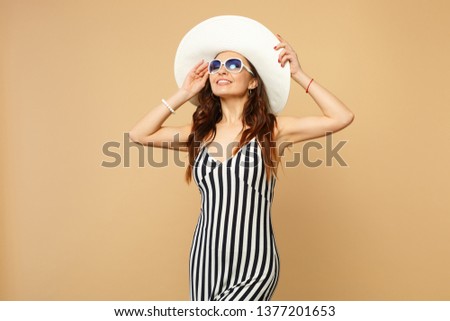 Tender young woman in black and white striped dress, hat and sunglasses keeping eyes closed isolated on pastel beige wall background. People sincere emotions, lifestyle concept. Mock up copy space