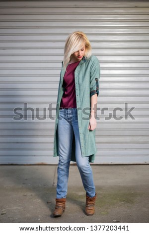 Portrait of beautiful fashionable long blonde hair girl while she is posing wearing elegant dress standing on concrete in front of street background
