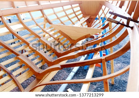 Small wooden boat in a boatyard. Structure with ribs, keel, bulkheads and longitudinal members. A wood clamp visible.