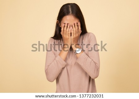 Sad young Asian woman cry with palm to face  on beige background