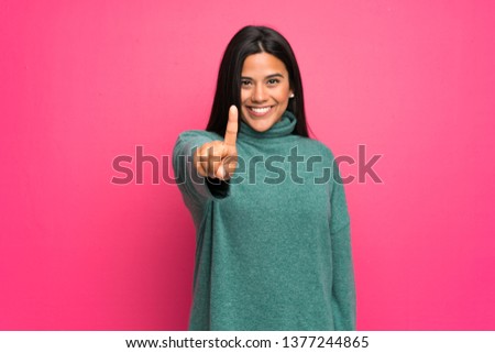 Young Colombian girl with green sweater showing and lifting a finger