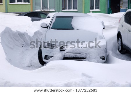 Сar covered with snow stands in the parking lot of residential building in winter. Сoncept of bad weather, snowfall, harsh weather conditions, frost, blizzard, car engine did not start