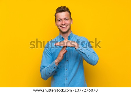 Blonde man over isolated yellow wall making time out gesture
