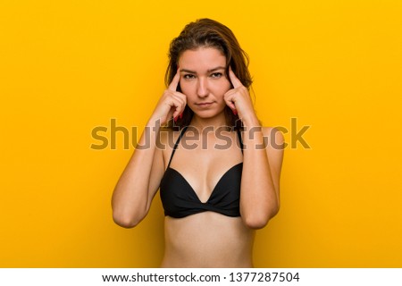 Young european woman wearing bikini focused on a task, keeping her forefingers pointing head.