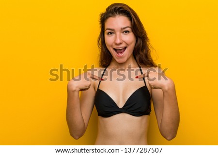 Young european woman wearing bikini surprised pointing at herself, smiling broadly.