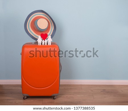 Travel and tourism concept. Orange suitcase on blue background wall with Icon of family and red heart. Sun hat on handle. Minimal style. Summer background. 