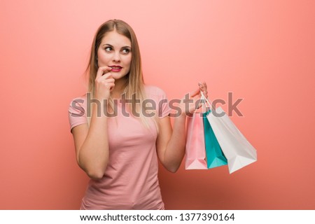 Young pretty russian girl relaxed thinking about something looking at a copy space. She is holding a shopping bags.