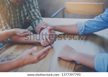 Two Christian people are praying for young man friends on wood table at church prayer room to encourage and support him in his problem and spiritual growth, small prayer group and fellowship concept
