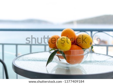 New harvest of tasty organic oranges and lemons, citrus fruits in glass bowl outside with sea view