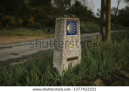 Camino de Santiago post made of stone, with yellow arrow and sign.