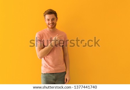 Young redhead man smiling and pointing to the side