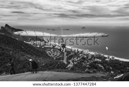 Black and white image of hang glider taking off over the beach and mountains in rio de janeiro