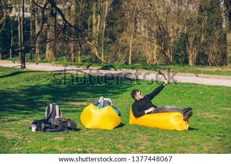 two men friends laying on yellow inflatable mattress reading books surfing internet. sunny spring day,