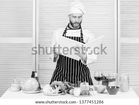 Man bearded chef cooking food. Guy read book recipes. Culinary arts concept. Man learn recipe. Improve cooking skill. Book family recipes. Ultimate cooking guide for beginners. According to recipe.