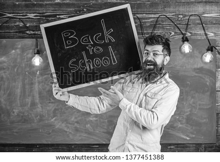 Teacher in eyeglasses holds blackboard with title back to school. Man with beard and mustache on happy face welcomes students, chalkboard on background. High school concept.