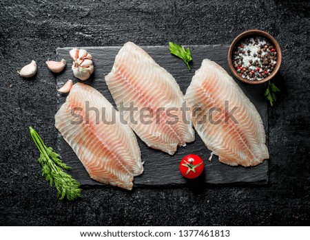 Fish fillet on black stone Board with dill, tomatoes and spices in bowl. On black rustic background