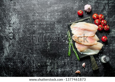 Tilapia fish fillet with tomatoes on a branch, rosemary, garlic and salt. On black rustic background