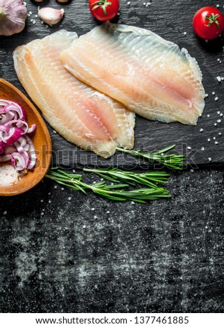 Fish fillet with chopped onion in bowl, garlic and rosemary. On black rustic background