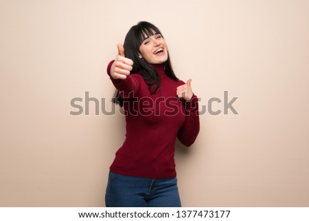 Young woman with red turtleneck giving a thumbs up gesture because something good has happened
