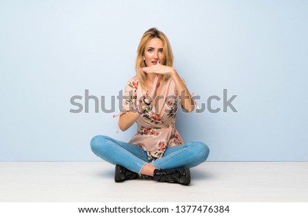 Young blonde woman sitting on the floor making time out gesture