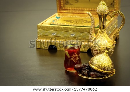 Still life with traditional luxury golden arabic coffee set with dallah, cup and dates. Quran book background. Ramadan concept.