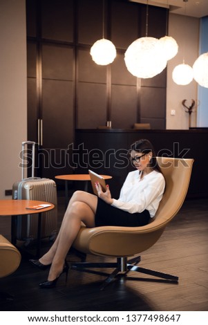 Confident businesswoman listening music on her tablet computer while sitting in chair in airport business lounge Royalty-Free Stock Photo #1377498647