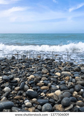 Beautiful multi-colored round stones on the sea, rivers, lakes, pond, ocean and boiling water with waves on the rocky beach of a tropical warm resort on the horizon and sky. Vertical view.