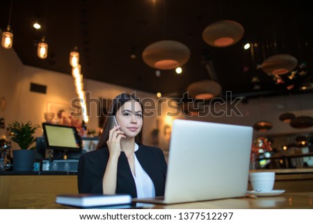 Serious woman proud CEO dressed in official wear having cellphone conversation during online training course via pc laptop computer while sitting in restaurant during business travel abroad. 