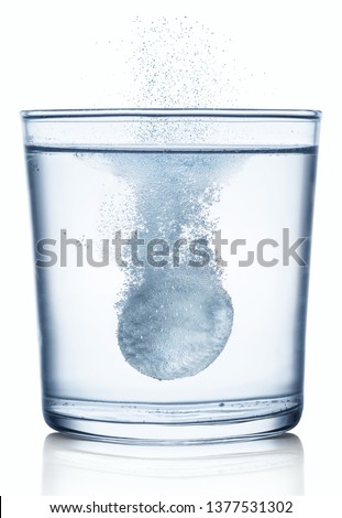 Effervescent tablet dissolving in a glass of water. Isolated on white background.