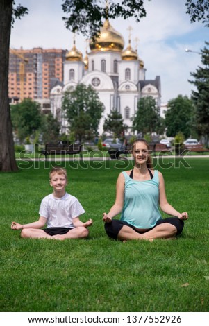 Pregnant woman sits in yoga posies and meditates with her son. Yoga, meditation and relax. Pregnancy and family. Lifestyle.