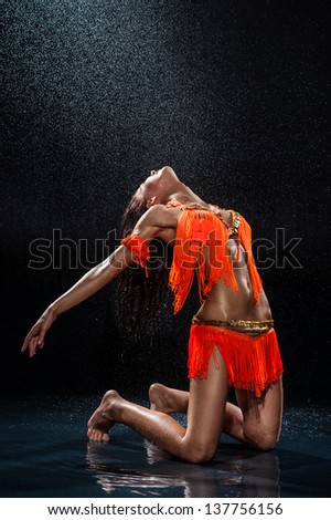 Woman dancing under rain in orange dress. Studio