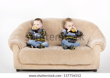 Twin brothers sitting on sofa in studio and drink juice from glases.